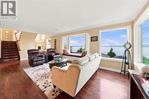 Living room with a sofa, chairs, bay window with a view, and hardwood floors. - 5287 Lost Lake Rd, Nanaimo