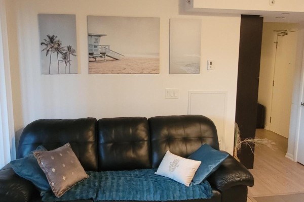 Living area with a black leather sofa, decorative pillows, and beach-themed wall art. - 529 - 830 Lawrence Avenue W, Toronto