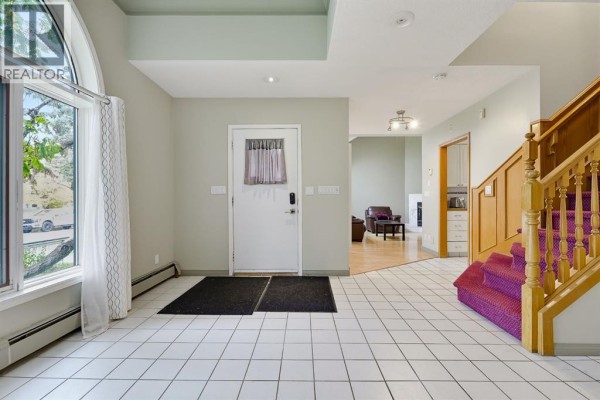 Foyer with white tiled floor, white door, and a wooden staircase with purple carpet. - 529 18 Avenue Nw, Calgary