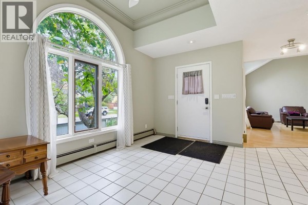 Foyer with white tiled floor, large arched window, white door, and access to the living area. - 529 18 Avenue Nw, Calgary
