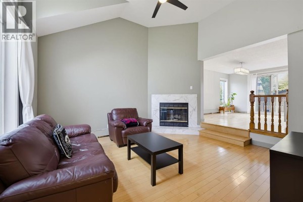 Living room with hardwood floors, brown leather sofa, armchair, coffee table, and marble fireplace. - 529 18 Avenue Nw, Calgary
