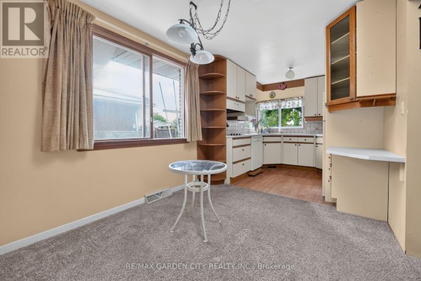 Kitchen area with a small round table, window with striped curtains, and beige carpet. - 529 Carlton Street, St  Catharines