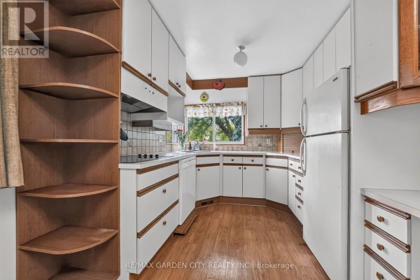 L-shaped kitchen with white cabinets, wooden accents, wood-look flooring, and a window. - 529 Carlton Street, St  Catharines