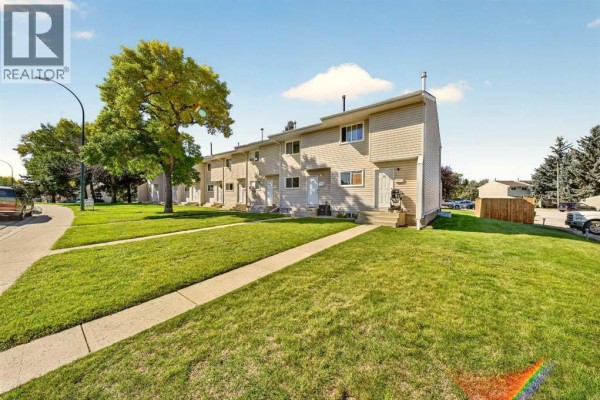 Side view of beige townhouses with green lawns and mature trees. - 53, 55 Lemoyne Crescent W, Lethbridge