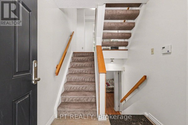 Entrance hallway with dark door, beige carpeted stairs, and wood banisters. - 53 - 110 Havelock Street, Ottawa