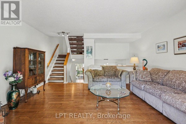 Living room with hardwood floors, patterned sofa, wooden china cabinet, and staircase. - 53 - 110 Havelock Street, Ottawa