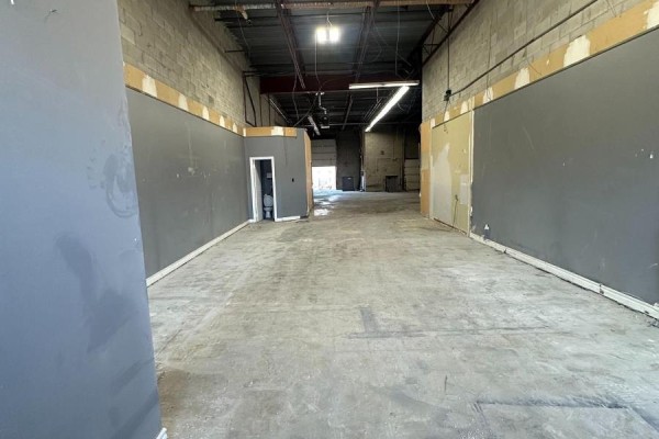Looking down a long, empty commercial space with gray walls, concrete floor, and garage door. - 53 - 173 Advance Boulevard, Brampton