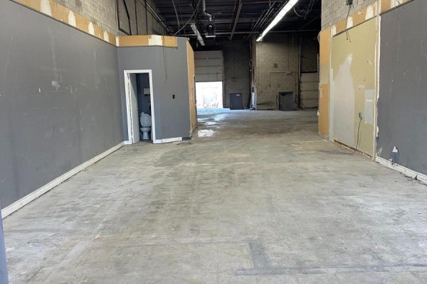 Empty commercial space with concrete floor, gray walls, a small bathroom, and garage door. - 53 - 173 Advance Boulevard, Brampton