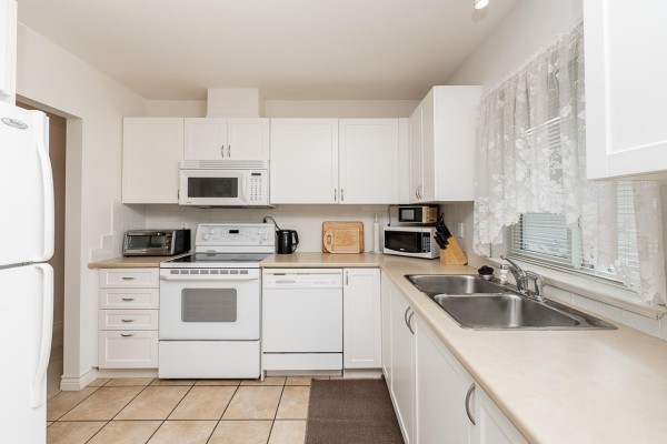 Kitchen with white cabinets, double sink, and a dining area with a wooden table and chairs. - 53 17516 4 Avenue, Surrey