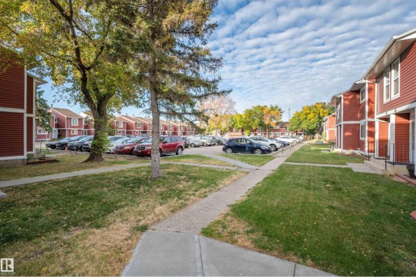 Exterior view of red vinyl-sided townhouses with green lawns and parking lot. - #53 4707 126 Av Nw, Edmonton