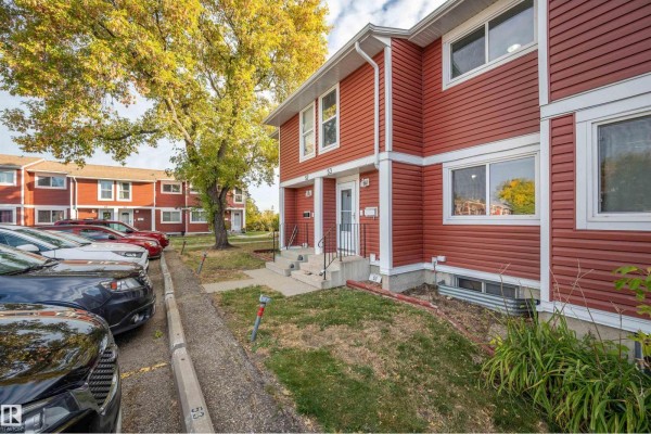 Close-up exterior view of red vinyl-sided townhouses with two windows and a door. - #53 4707 126 Av Nw, Edmonton