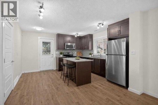 Kitchen with dark cabinets, granite island, stainless steel appliances, and a door. - 53 Cranford Way Se, Calgary