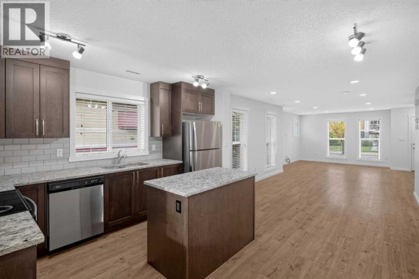 Kitchen with island, stainless steel appliances, and view to a bright living area. - 53 Cranford Way Se, Calgary