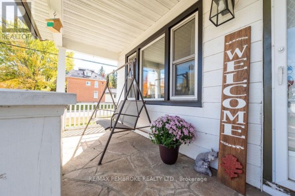 Front porch with stone flooring, white railings, and a swing seat, decorated with a welcome sign and flowers. - 53 Doran Street, Petawawa