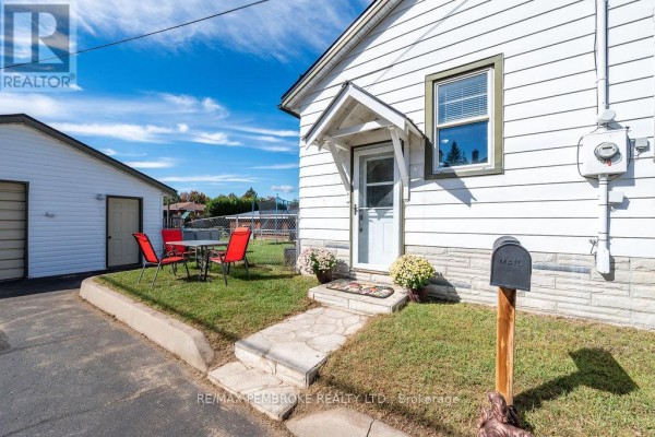 Entrance to a white house with a small porch, stone walkway, mailbox, and a detached garage with an outdoor seating area. - 53 Doran Street, Petawawa