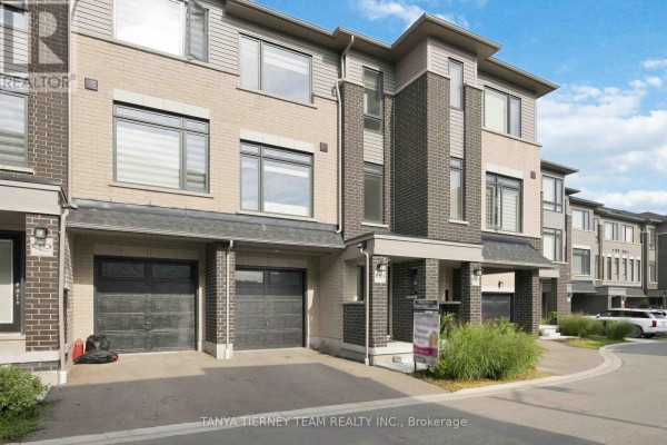 Close-up front view of a townhouse entrance with beige brick, dark grey brick, and two garages. - 53 Emmas Way, Whitby