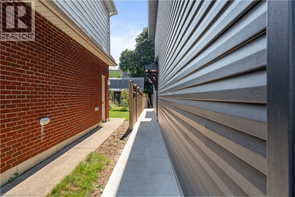 Exterior view of the narrow side yard between two houses with brick and vinyl siding. - 53 Franklin Street Unit# B, Brantford