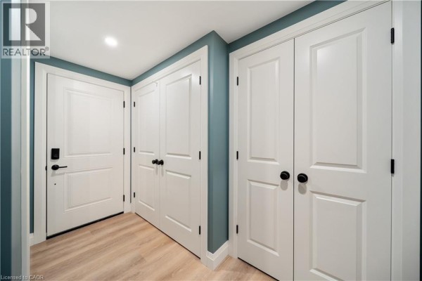 Hallway with light wood laminate flooring and multiple white doors, including a front entrance door. - 53 Franklin Street Unit# B, Brantford