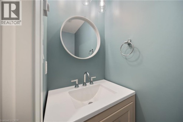 Powder room with a white vanity, sink, chrome faucet, and round mirror on a teal wall. - 53 Franklin Street Unit# B, Brantford