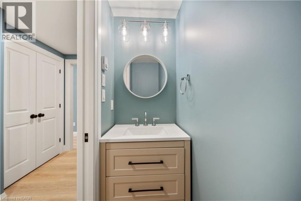 Hallway view of a powder room with a vanity and sink, next to a closet door. - 53 Franklin Street Unit# B, Brantford