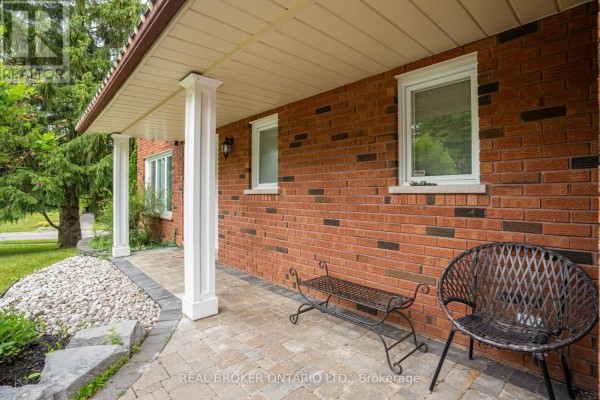 Covered front porch with brick walls, white columns, a bench, and a chair. - 53 Marilyn Street, Caledon