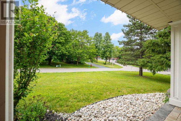 View of a grassy front yard and mature trees from under the covered porch. - 53 Marilyn Street, Caledon