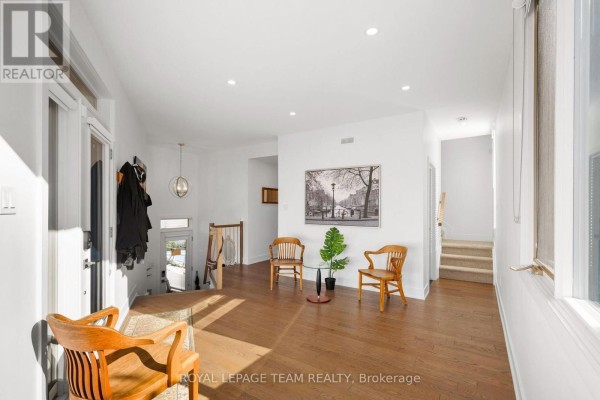 Interior foyer with hardwood floors, two wooden chairs, a plant, and artwork on the wall. - 53 Merton Street, Ottawa