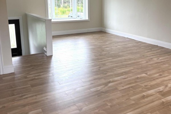 Living area with light wood laminate flooring and a white railing next to stairs. - 53 Mood Road, Pleasant Lake