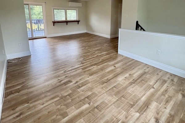 Living area with light wood laminate flooring, a window, and a sliding glass door. - 53 Mood Road, Pleasant Lake