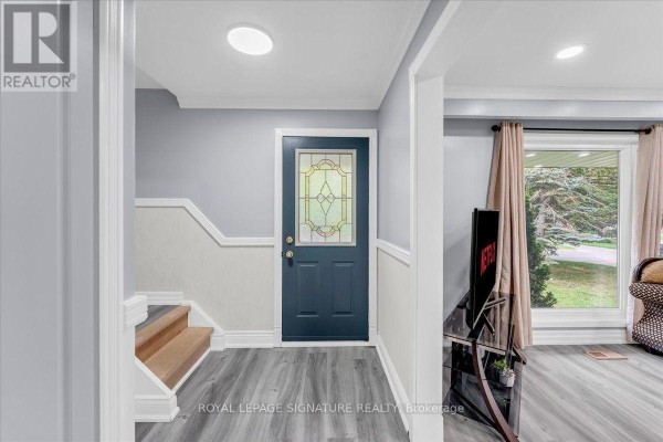 Interior entryway with a dark blue front door, wood stairs, and grey wood-look flooring. - 530 Brentwood Avenue, Oshawa