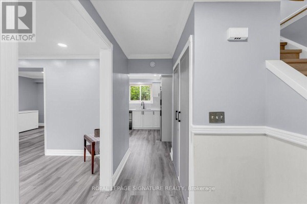 Hallway with light blue walls, grey flooring, a wooden bench, and a view into a white kitchen. - 530 Brentwood Avenue, Oshawa
