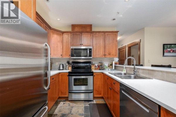 Corner kitchen with stainless steel refrigerator, light wood cabinets, and quartz countertops. - 5300 Big White Road Unit# 105, Big White