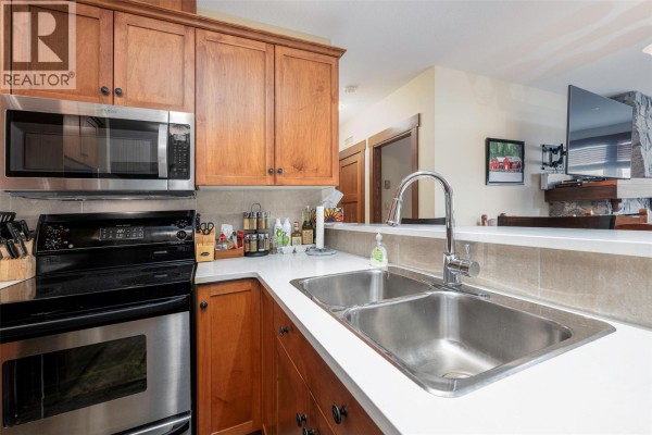 Kitchen with double sink, stainless steel faucet, wood cabinets, and a breakfast bar. - 5300 Big White Road Unit# 105, Big White