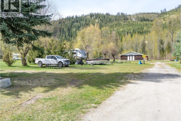 View of a campsite with RVs, a pickup truck, a boat, and picnic tables with a wooded hill backdrop. - 5301(2-10)-5317-5323-5327 Prosh Frontage Road, Craigellachie