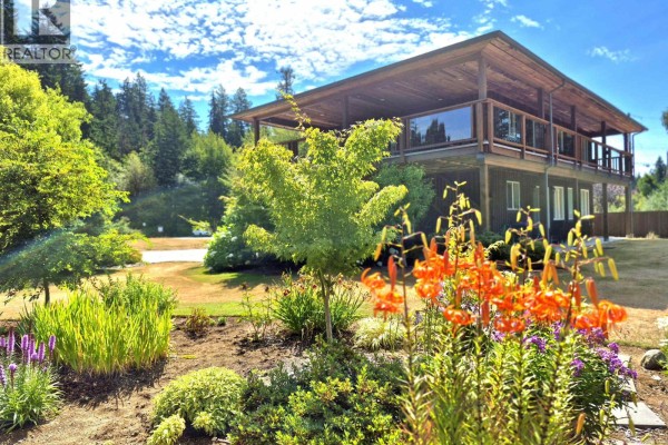 View of the upper wooden deck and lower level of a house, framed by lush green trees and orange flowers. - 5301 Stamford Place, Sechelt