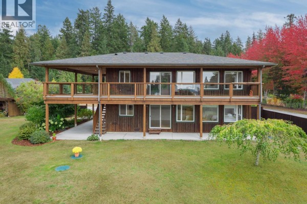 Rear exterior of a wood-sided house with a wrap-around deck, visible from a grassy lawn. - 5301 Stamford Place, Sechelt