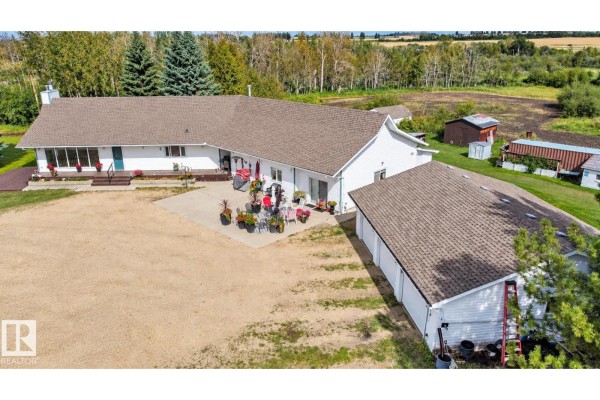 Aerial view of the back of the white house with a patio, garage, and surrounding landscape. - 53027 Rge Road 225, Rural Strathcona County