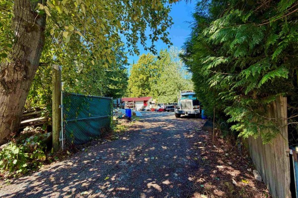 Chain-link gate opens to gravel driveway with sheds, containers, and a large truck. - 5307 246a Street, Langley