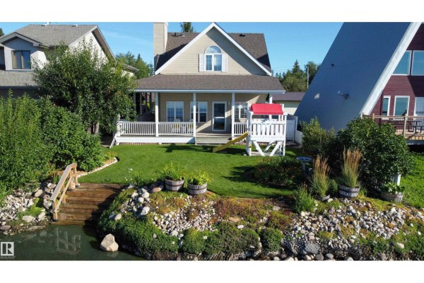 Backyard of a beige house with a covered porch, lawn, and lake access stairs. - 5309 51 Av, Rural Lac Ste  Anne County