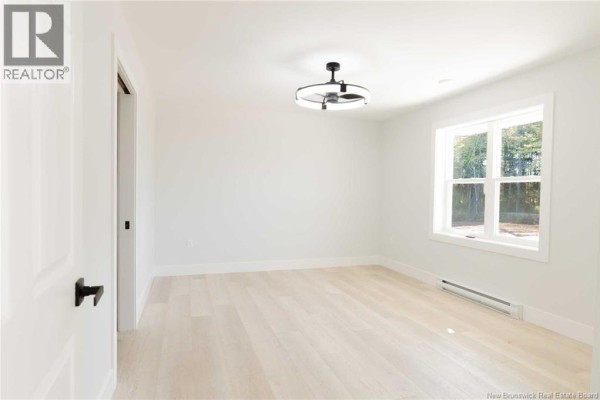 Empty room with light gray walls, white trim, wood-look flooring, and a large window. - 531 Chem. Ward Road, Bouctouche