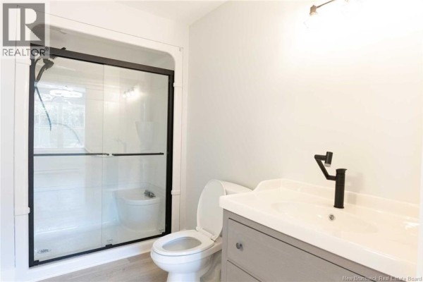 Bathroom with a white toilet, gray vanity, white sink, black faucet, and a glass-enclosed shower. - 531 Chem. Ward Road, Bouctouche