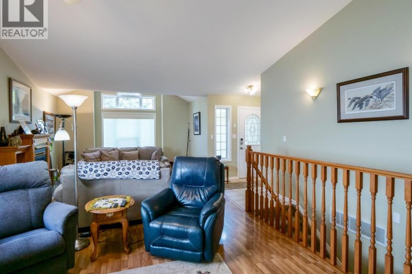 Living room with blue recliner, sofa, wood railings, and view towards the front door. - 531 Dawson Street, Quesnel
