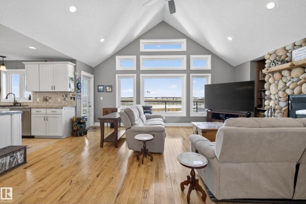 Living room with vaulted ceiling, stone fireplace, and large windows overlooking a rural landscape. - 531064 Range Road 174, Rural Lamont County