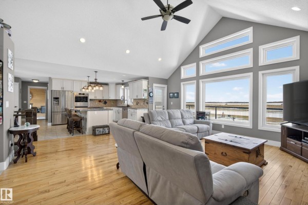 Open-concept living room and kitchen with vaulted ceilings, large windows, and a stone fireplace. - 531064 Range Road 174, Rural Lamont County