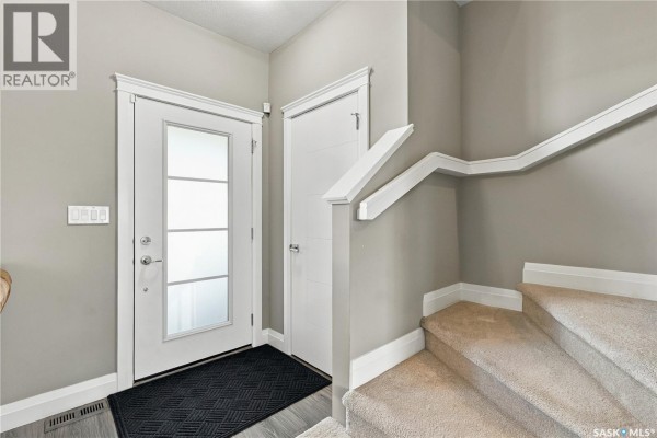 Entrance foyer with glass front door, black mat, and beige carpeted stairs. - 5313 Green Silverberry Drive E, Regina