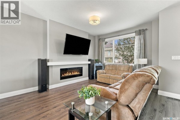 Living room with grey walls, a large TV over a modern fireplace, and brown sofas. - 5313 Green Silverberry Drive E, Regina