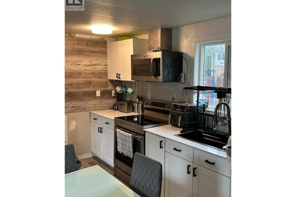 Kitchen with white cabinets, stainless steel appliances, wood-look backsplash, and laminate flooring. - 5317 Freda Avenue, Kamloops