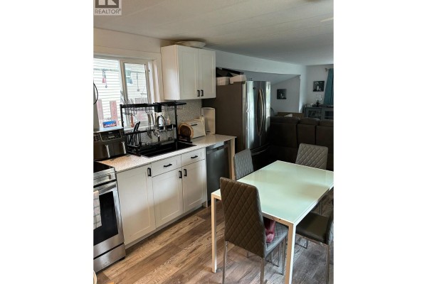 Kitchen and dining area with white cabinets, stainless steel refrigerator, and a glass-top dining table. - 5317 Freda Avenue, Kamloops