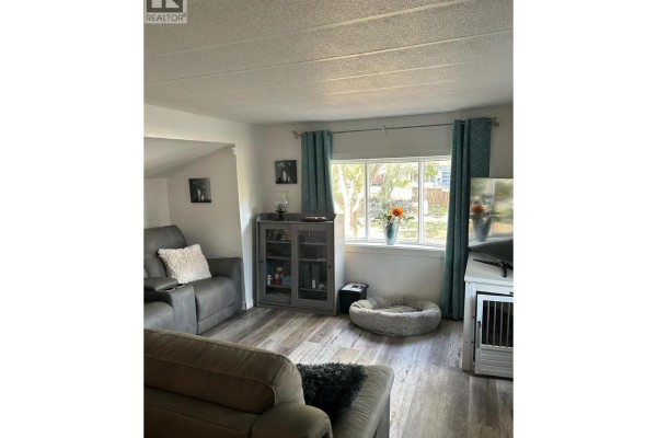Living room with gray sofas, a television, a glass-front cabinet, and a dog bed by the window. - 5317 Freda Avenue, Kamloops