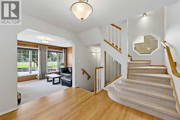 Main floor entryway and staircase with an arched doorway leading to a living room with large windows. - 532 54 Avenue Sw, Calgary